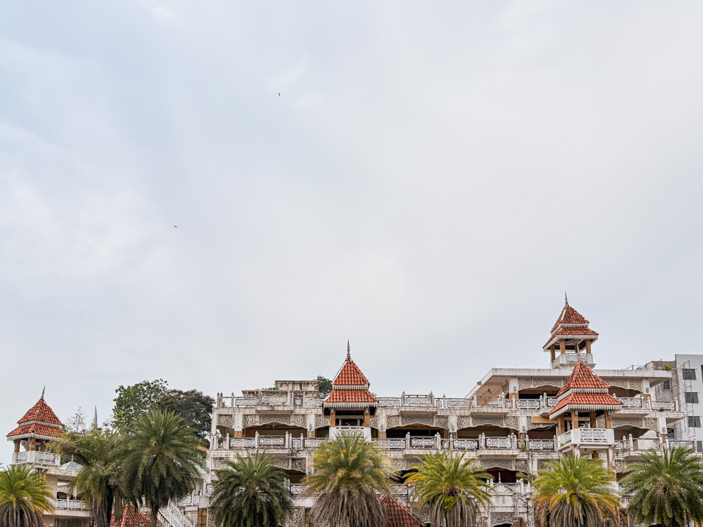 A shuttered market building with complex balconies and turrets rises above a row of palm trees