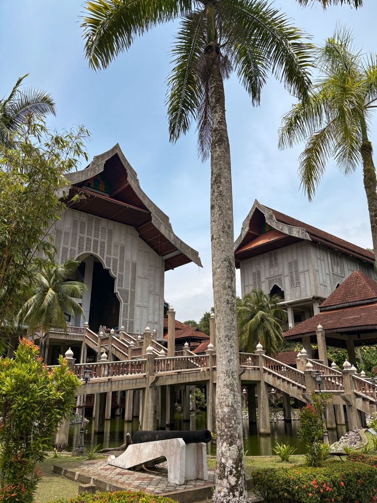 The Terengganu state museum rises high on stilts above a pond with palm trees in the foreground